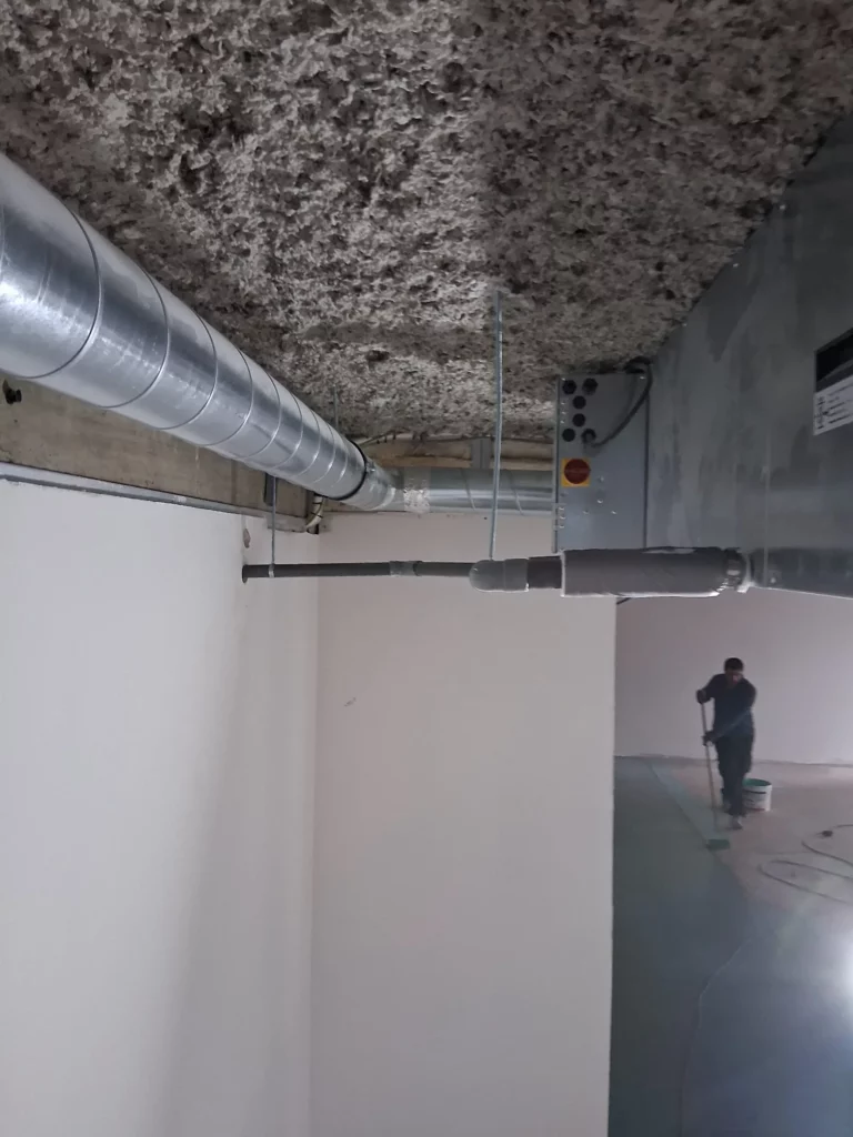 Technicien installant un conduit de VMC double-flux au plafond d'une crèche à Evian.