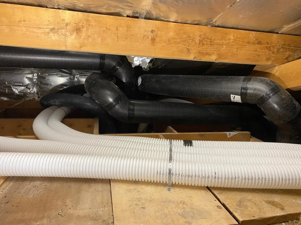 Installation de conduits VMC double flux isolés et gaines flexibles blanches sous une charpente en bois.
